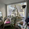 A balcony decorated with plants and cushions, featuring sheer curtains and a view of buildings. Produktbild-Vorschau