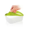 A hand is shown lifting the lid off a transparent food storage container with a green lid. Podgląd zdjęcia produktu