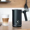 A black milk frother sits on a wooden countertop next to a glass of layered coffee. Produktbild-Vorschau