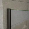 A close-up view of a shower enclosure corner, showing a metallic profile and a green line representing the glass edge against a tiled wall. Produktbild-Vorschau