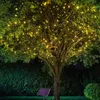 A tree decorated with string lights at night, with a birdhouse attached to a branch. Produktbild-Vorschau
