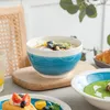 A table setting with various dishes and bowls, including a salad bowl, a bowl of green soup, and a plate with a waffle-like item topped with tomatoes and blueberries. Produktbild-Vorschau