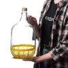 A person is holding a large glass bottle with a yellow protective base. Voir les images du produit