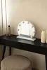 A vanity table with a round makeup mirror with lights, a stool, and some cosmetic bottles. Podgląd zdjęcia produktu