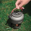 A hand holding a camping kettle over a small stove on grass. Produktbild-Vorschau
