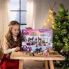 A young girl is holding an advent calendar with horses and winter scenery on it, with a Christmas tree in the background. Produktbild-Vorschau