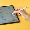 A hand holding a stylus pen and writing on a tablet screen, with a yellow background. Voir les images du produit