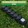A black outdoor power strip with multiple outlets is lying on wet grass. Produktbild-Vorschau