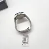 A watch is placed on a white surface with a black box in the background. Produktbild-Vorschau