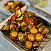 A close-up view of grilled vegetables and potatoes in a metal grill basket. Náhled obrázku produktu