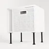 A white storage unit with a woven front panel, supported by four black legs, against a white background. Produktbild-Vorschau