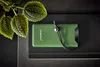 A green power bank with a black lanyard is placed on a black notebook, with green leaves in the upper left corner. Voir les images du produit