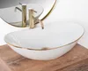 A white oval vessel sink with a gold rim and a gold faucet, placed on a wooden surface. Podgląd zdjęcia produktu