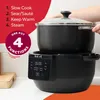 A person is placing the lid on a black multi-cooker appliance, which is sitting on its base. The base has a digital display showing the time. Text overlays highlight the product's features. Produktbild-Vorschau