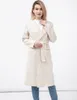 A woman wearing a cream-colored coat and blue jeans stands against a white background. Produktbild-Vorschau