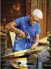 An older man is using a cordless drill to screw into a piece of wood, which is supported by a workbench. Produktbild-Vorschau