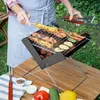 A person is grilling skewers and vegetables on a portable charcoal grill outdoors. Náhled obrázku produktu
