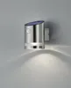 A silver, cylindrical solar-powered wall light with a motion sensor is mounted on a light gray wall, casting a downward light pattern. Produktbild-Vorschau