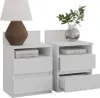 Two white nightstands are shown side-by-side against a white background. The left nightstand has a lamp and books on it, while the right nightstand has a vase with greenery and books. One drawer on the right nightstand is partially open. Náhľad obrázku produktu