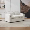 A beige sofa bed with two pillows is shown in a room with a painting on the wall and shelves in the background. Produktbild-Vorschau