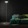 A floor lamp stands next to a green sofa with decorative pillows and a throw blanket. Produktbild-Vorschau