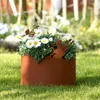 A rusty metal planter with a fairy and butterfly motif, filled with white daisies, sits on a green lawn. Produktbild-Vorschau