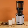 A Kuvings slow juicer is shown next to two glasses of milk and some cookies, with almonds scattered around. Produktbild-Vorschau