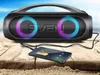 A portable speaker and a smartphone are placed on a wooden surface with sand and a beach background. Produktbild-Vorschau