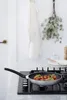 A frying pan with food is on a stovetop, with kitchen decor in the background. Voir les images du produit