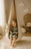 A young girl is sitting in a hanging chair and reading a book. There is a stuffed bunny in a pocket on the side of the chair. The room has a fluffy rug and a wicker chair in the background. Produktbild-Vorschau