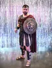 A man dressed in a gladiator costume stands in front of a shimmering silver background. Podgląd zdjęcia produktu