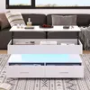 A white coffee table with LED lighting is shown in a living room setting, placed in front of a sofa. Náhľad obrázku produktu
