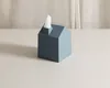 A blue house-shaped tissue box with a tissue emerging from the chimney sits on a light gray surface in front of a beige curtain. Anteprima dell’immagine prodotto