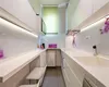 A modern, narrow kitchen with white cabinets and countertops, featuring under-cabinet lighting and a window with a green blind. Produktbild-Vorschau