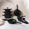 A set of black cookware and kitchen utensils arranged on a light-colored surface against a neutral background. Anteprima dell’immagine prodotto