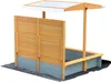 A wooden sandbox with a canopy, shown outdoors on a dark ground cover. Produktbild-Vorschau