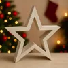 A wooden star decoration is placed in front of a blurred Christmas tree with lights and ornaments, and a red stocking hanging in the background. Produktbild-Vorschau