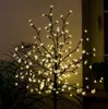 A decorative LED tree with warm white lights shaped like flowers, set against a dimly lit indoor background with some greenery. Produktbild-Vorschau