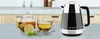A black and silver electric kettle is shown on a countertop next to a teapot, a cup of tea, a lemon slice, and sugar cubes. Náhled obrázku produktu