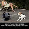 A woman sits in a chair reading a book and holding a drink on a wooden deck, while a dog lies on the deck near a misting fan. Náhľad obrázku produktu