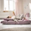 A young girl is lying on a floor cushion, reading a book, with a stuffed bunny next to her. Anteprima dell’immagine prodotto