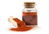 A glass jar filled with red powder, with a wooden scoop next to it, also filled with the powder and some spilled on a white surface. Produktbild-Vorschau