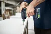 A person is using a cordless drill to screw into a white surface in what appears to be a workshop or construction environment. Voir les images du produit
