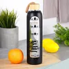 A glass water bottle with time markings is placed on a wooden cutting board, next to an orange and lemons, with a potted plant and a towel in the background. Voir les images du produit