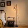 A bedroom scene with a bed, nightstand, and a floor lamp. Produktbild-Vorschau