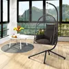 A hanging egg chair with a cushion is placed next to a small white table with a vase of flowers and some teacups, in a room with large windows overlooking a forest. Produktbild-Vorschau