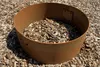 A rusty metal ring filled with wood chips, sitting on a surface of wood chips. Produktbild-Vorschau