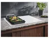 A white induction cooktop with a grilling pan containing food is shown on a granite countertop. Voir les images du produit
