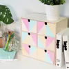 A wooden drawer unit with geometric pastel patterns, placed on a white desk next to art supplies and books. Produktbild-Vorschau