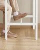 A close-up of a person's legs and feet wearing boat shoes and white socks, with one foot resting on a white structure. Náhled obrázku produktu